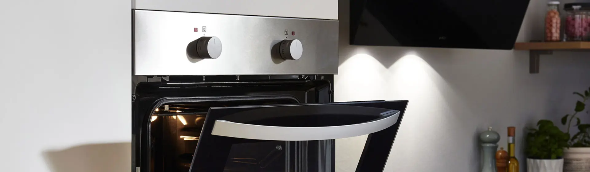 Moderne Küche mit Edelstahlofen, Tür angelehnt, zwei Bedienknöpfen, Licht im Inneren. Schlichtes, minimalistisches Dekor mit Gewürzgläsern auf einem Regal Moderne Küche mit Edelstahlofen, Tür angelehnt, zwei Bedienknöpfen, Licht im Inneren. Schlichtes, minimalistisches Dekor mit Gewürzgläsern auf einem Regal